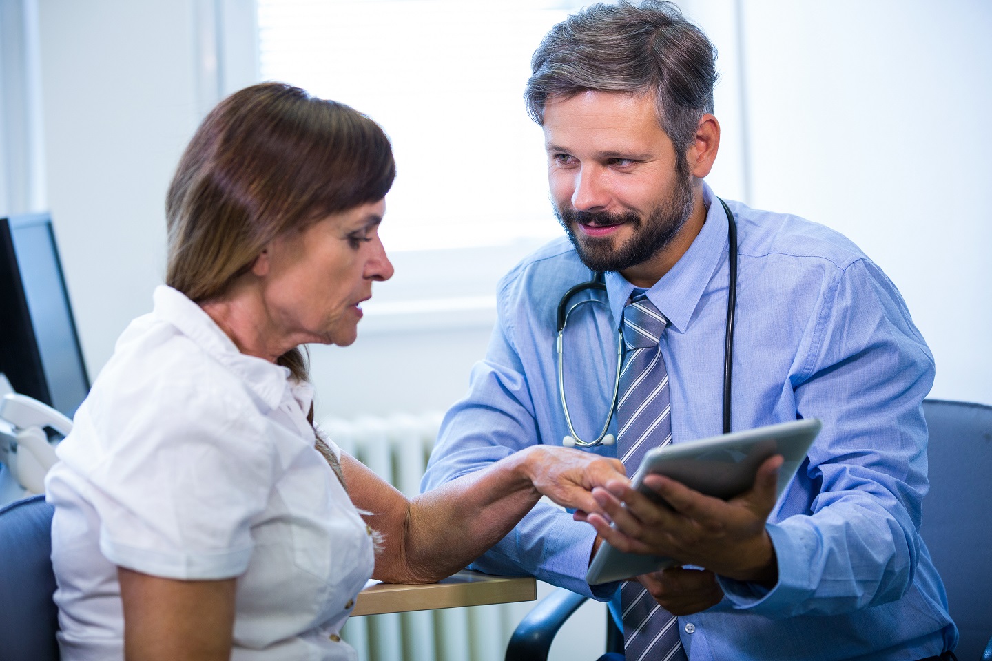 Male doctor discussing with patient over digital tablet at the hospital